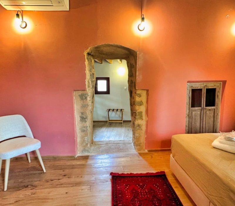 Chloe Junior Suite bedroom with an orange wall and stone doorway to the bathroom
