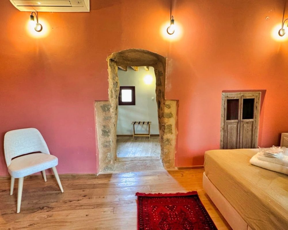 Chloe Junior Suite bedroom with an orange wall and stone doorway to the bathroom